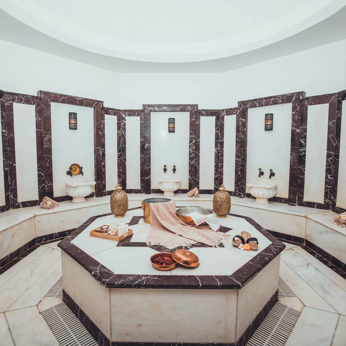 Sala hammam in marmo bianco e scuro con bacinelle in ottone