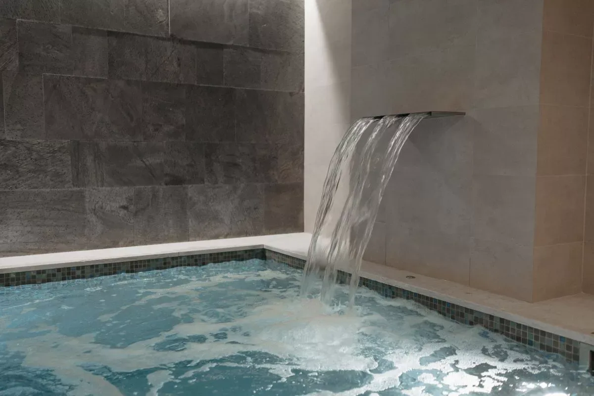 Vasca termale con cascata d'acqua e pareti in pietra naturale in un centro benessere
