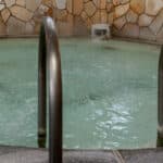piccola piscina termale tonda in primo piano la scaletta sullo sfondo una parete in pietre