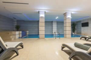ambiente termale chiuso si vedono 3/4 sdraie 2 colonne e in lontananza si intravede la piscina